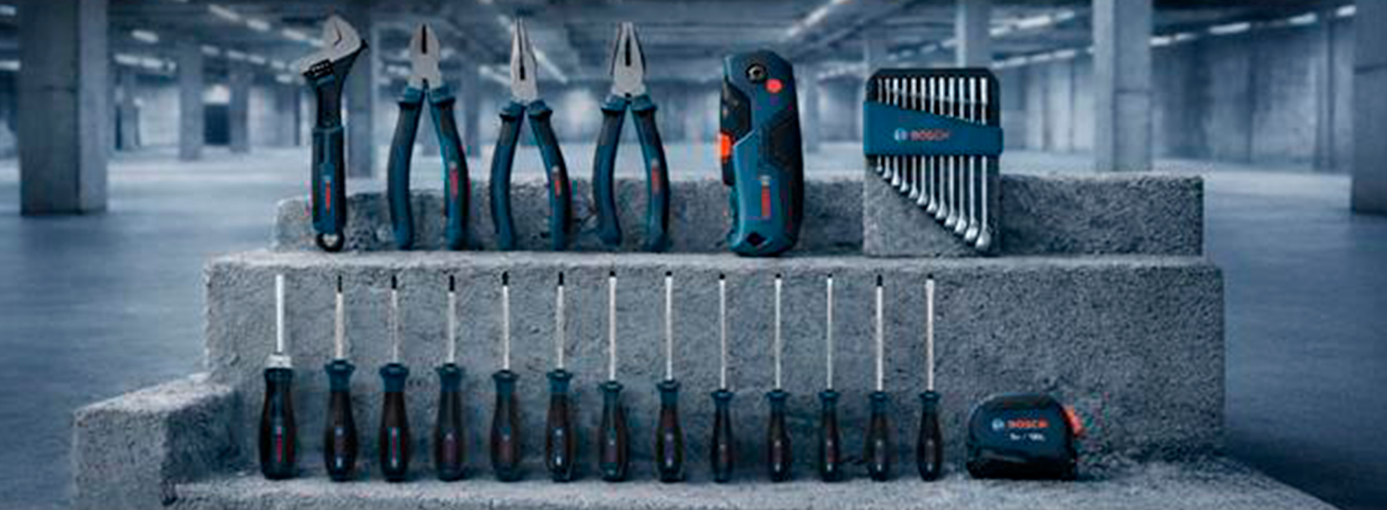 Uma coleção de ferramentas Bosch Professional em um degrau de concreto, incluindo alicates, chaves de fenda e uma ferramenta multifuncional, todas em azul e preto.
