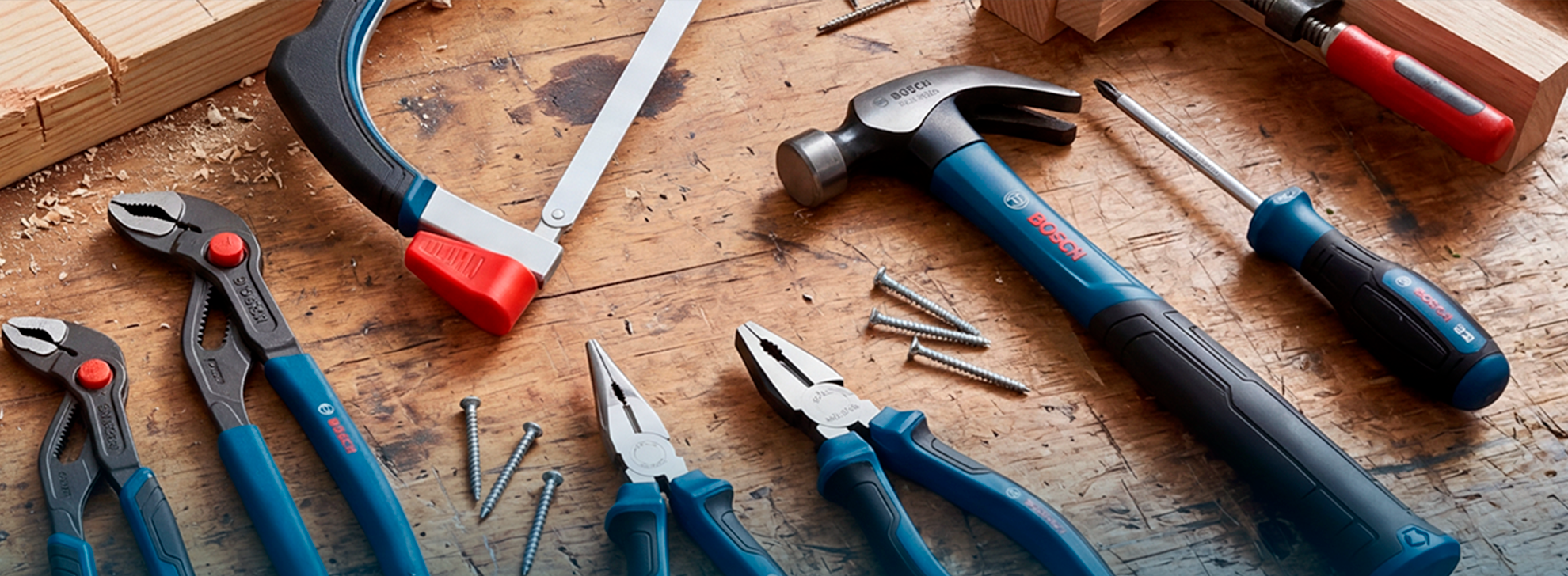 Uma seleção de ferramentas Bosch Professional, incluindo alicates, um martelo, uma chave de fenda e uma serra, dispostas em uma bancada de madeira com parafusos e lascas de madeira espalhadas.