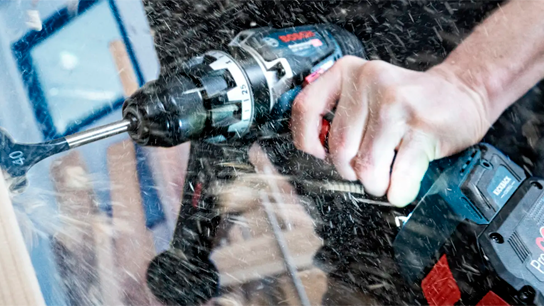 Uma furadeira Bosch Professional é usada em madeira, com serragem voando ao redor.