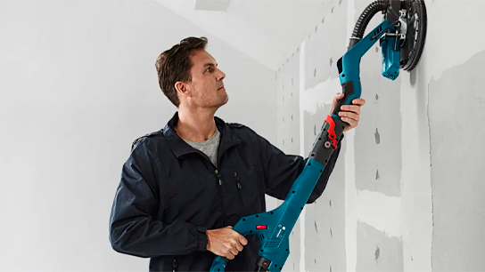 Um homem usa uma lixadeira de drywall Bosch Professional em uma parede.