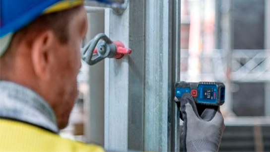 Um trabalhador utiliza uma ferramenta de medição Bosch Professional em uma estrutura de metal.