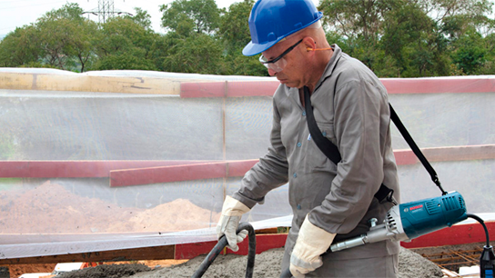 Um homem com um capacete azul usa uma ferramenta Bosch em um canteiro de obras.