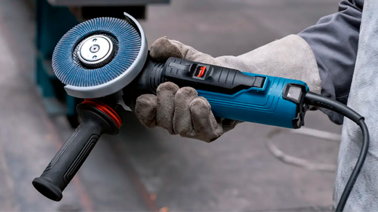 Uma esmerilhadeira angular azul Bosch Professional segurada em uma mão com luva.