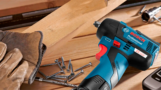 Uma furadeira sem fio Bosch Professional azul sobre madeira com parafusos e luvas.