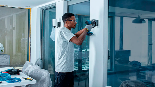 Um trabalhador usando uma ferramenta Bosch para perfurar uma parede em um espaço de escritório moderno.