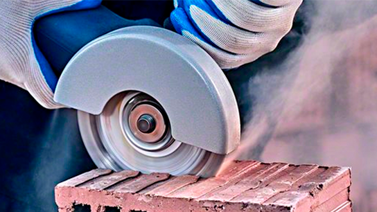 Uma serra manual corta um tijolo, emitindo poeira e faíscas.