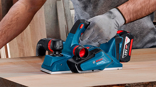 Um plano de madeira, um trabalhador utiliza um desengrossador Bosch Professional.