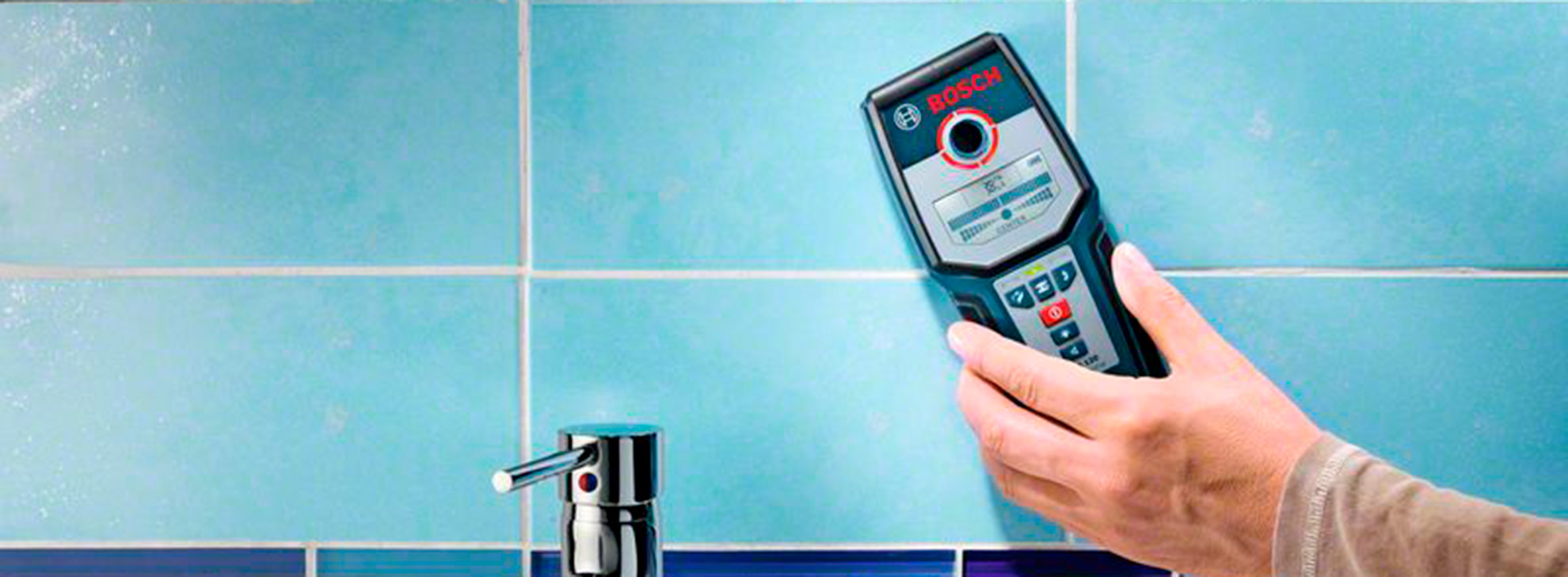 Uma ferramenta de medição Bosch Professional é segurada perto de uma torneira contra azulejos azuis.