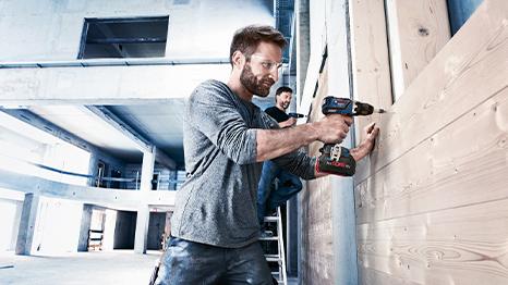 Um homem usa uma furadeira Bosch Professional em painéis de madeira em um canteiro de obras.