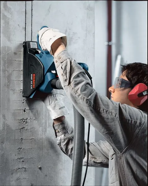 Uma pessoa usando equipamento de segurança usa um perfurador de parede para cortar um canal no concreto.