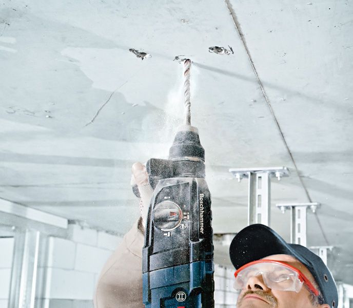 Uma pessoa usando equipamento de segurança perfura um teto de concreto.