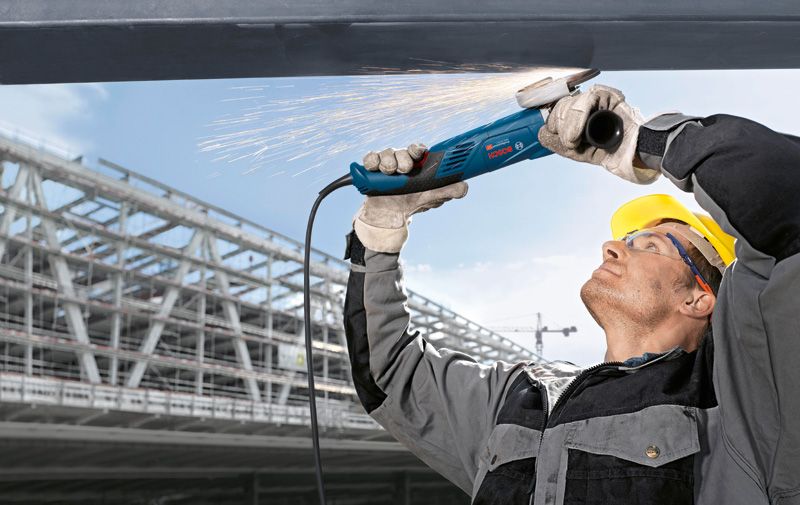 Uma pessoa usando equipamento de segurança tritura metal acima da cabeça, produzindo faíscas.