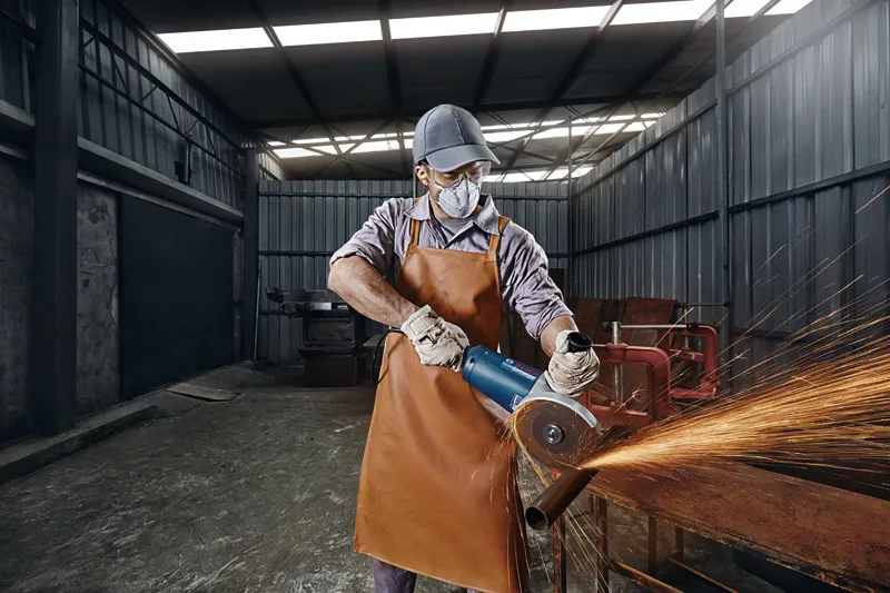 Uma pessoa usando equipamento de segurança corta um cano de metal com uma esmerilhadeira angular, provocando faíscas.