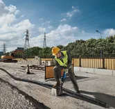 Uma pessoa usando equipamento de segurança usa uma serra alternativa para cortar um cano em um canteiro de obras.