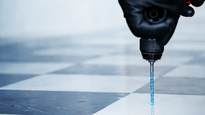 Pessoa usando equipamento de segurança perfura um piso de ladrilho.