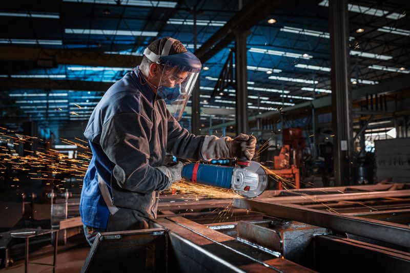 Uma pessoa usando equipamento de segurança esmerilha metal com uma esmerilhadeira angular em uma fábrica.
