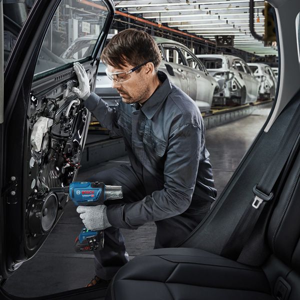 Uma pessoa usando equipamento de segurança usa uma ferramenta elétrica para montar uma porta de carro em uma fábrica.