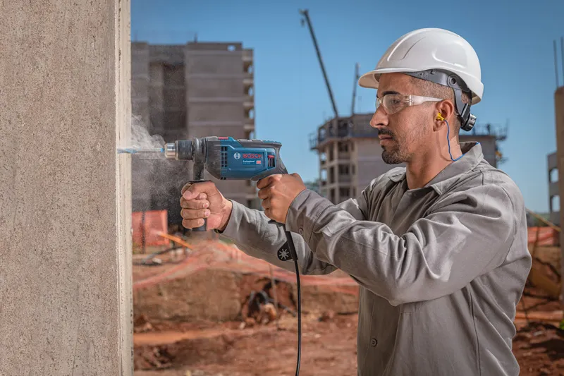Pessoa usando equipamento de segurança perfura uma parede de concreto em um canteiro de obras.