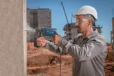 Pessoa usando equipamento de segurança perfura uma parede de concreto em um canteiro de obras.