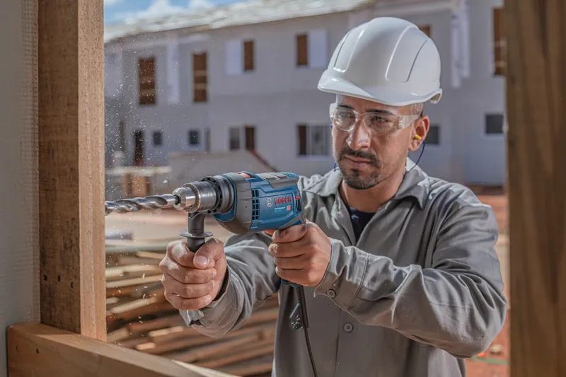 Uma pessoa usando equipamento de segurança perfura madeira em um canteiro de obras.