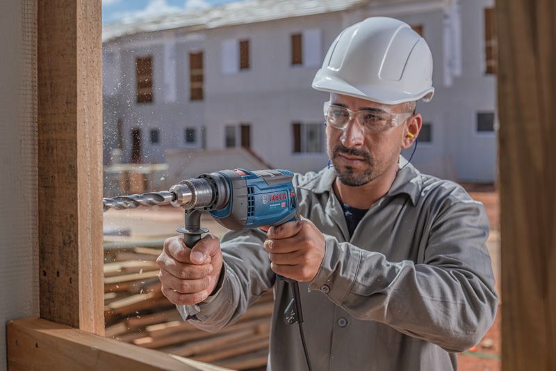 Uma pessoa usando equipamento de segurança perfura madeira em um canteiro de obras.