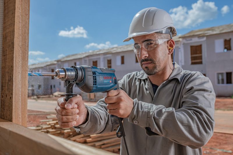 Uma pessoa usando equipamento de segurança perfura madeira em um canteiro de obras.