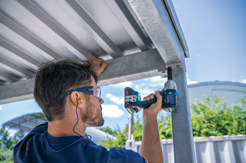 Pessoa usando equipamento de segurança usa chave de impacto sem fio em uma estrutura de metal.