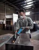 Uma pessoa usando equipamento de segurança tritura metal dentro de uma oficina industrial.