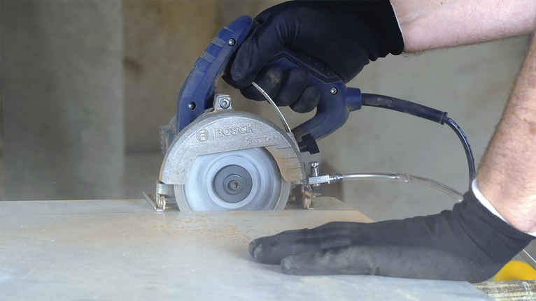Uma pessoa usando equipamento de segurança usa uma serra circular para cortar um azulejo.