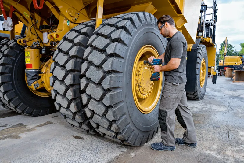 Uma pessoa usando equipamento de segurança usa uma chave de impacto em um pneu grande de veículo de construção.