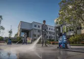 Duas pessoas usando equipamentos de segurança limpam o pavimento ao ar livre usando uma lavadora de alta pressão.