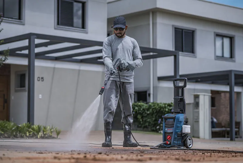Uma pessoa usando equipamento de segurança limpa uma entrada de automóveis com uma lavadora de alta pressão.