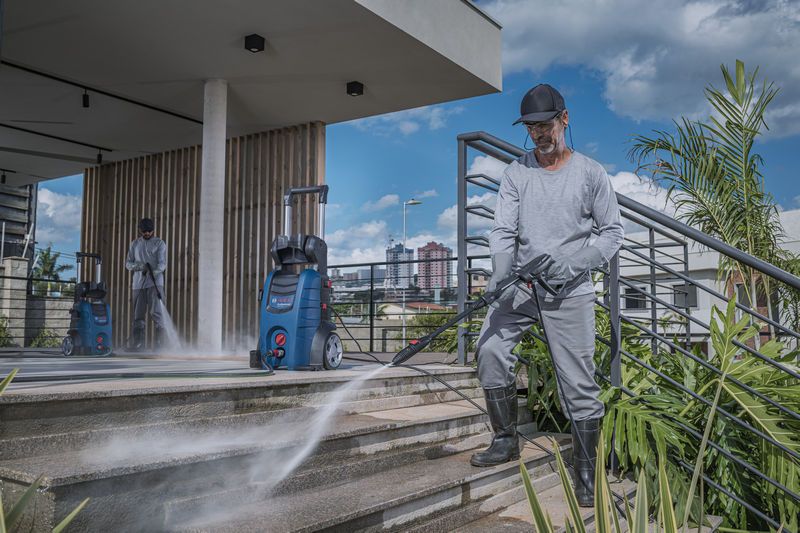 Uma pessoa usando equipamento de segurança usa uma lavadora de alta pressão para limpar escadas externas.