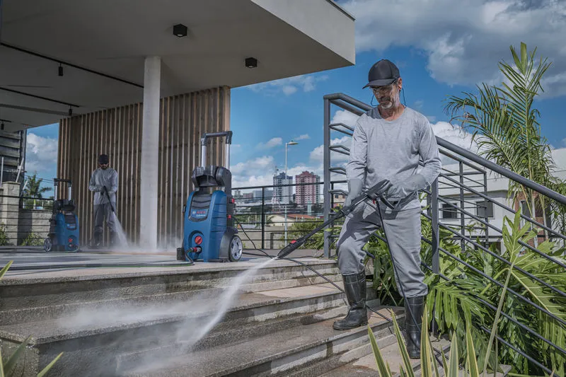 Uma pessoa usando equipamento de segurança usa uma lavadora de alta pressão para limpar escadas externas.