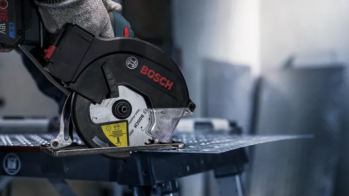 Uma pessoa usando equipamento de segurança corta uma chapa de metal com uma serra circular.