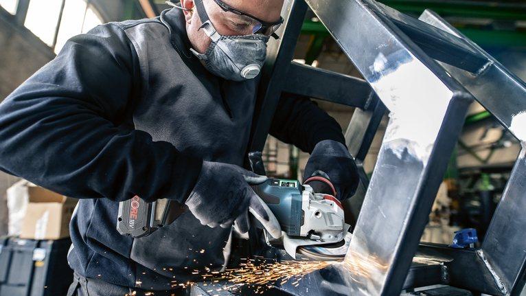 Uma pessoa usando equipamento de segurança tritura uma estrutura de metal, produzindo faíscas.