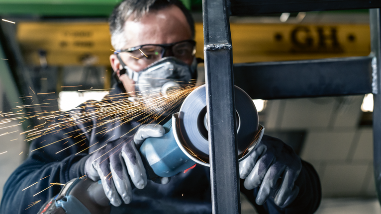 Uma pessoa usando equipamento de segurança tritura metal, criando faíscas.