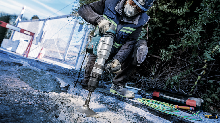 Uma pessoa usando equipamento de segurança perfura o pavimento em um canteiro de obras.