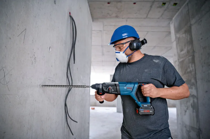 Uma pessoa usando equipamento de segurança perfura uma parede de concreto com um martelo rotativo.