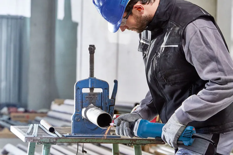 Uma pessoa usando equipamento de segurança usa uma retificadora reta para trabalhar em um tubo de metal.