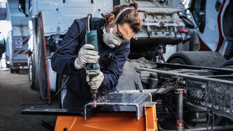 Uma pessoa usando equipamento de segurança tritura metal, produzindo faíscas em uma oficina.