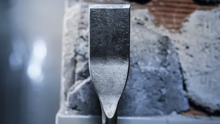 Broca de cinzel posicionada contra uma parede de concreto danificada.