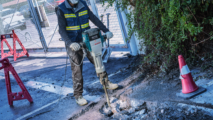 Uma pessoa usando equipamento de segurança quebra concreto com uma ferramenta de demolição elétrica.