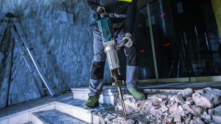 Uma pessoa usando equipamento de segurança usa um martelo de demolição para quebrar escadas de concreto.