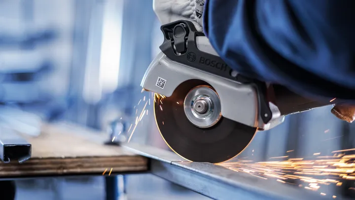 Uma pessoa usando equipamento de segurança corta metal com uma serra circular, criando faíscas.