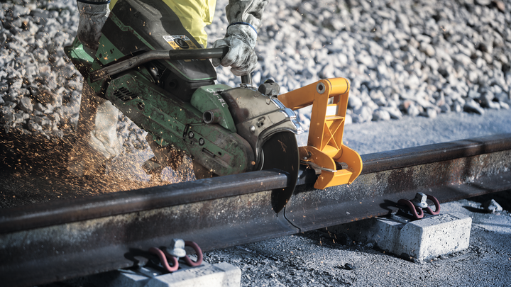 Uma pessoa usando equipamento de segurança corta um trilho de trem com uma serra elétrica.