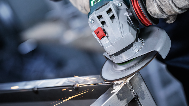 Uma pessoa usando equipamento de segurança tritura uma estrutura de metal, produzindo faíscas.