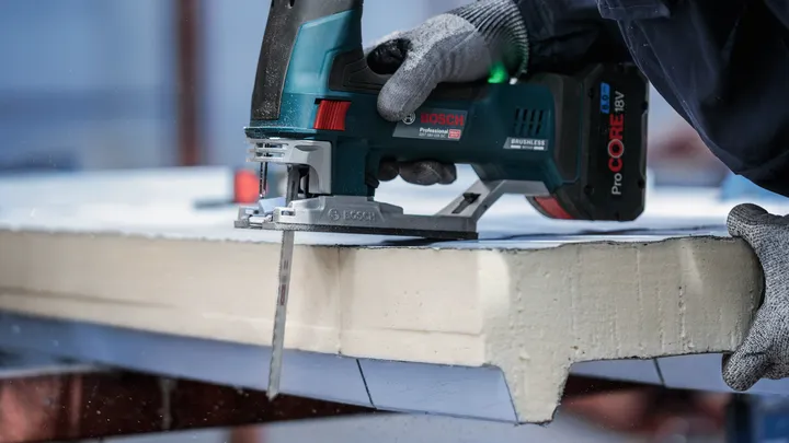 Uma pessoa usando equipamento de segurança corta uma placa de espuma com uma serra tico-tico sem fio.