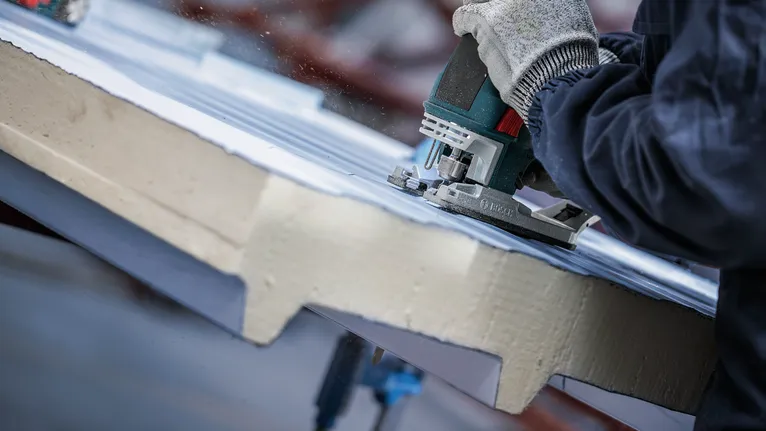 Uma pessoa usando equipamento de segurança corta material isolante com uma serra tico-tico.