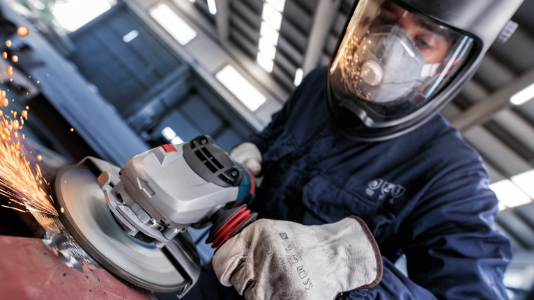 Uma pessoa usando equipamento de segurança tritura metal, provocando faíscas.